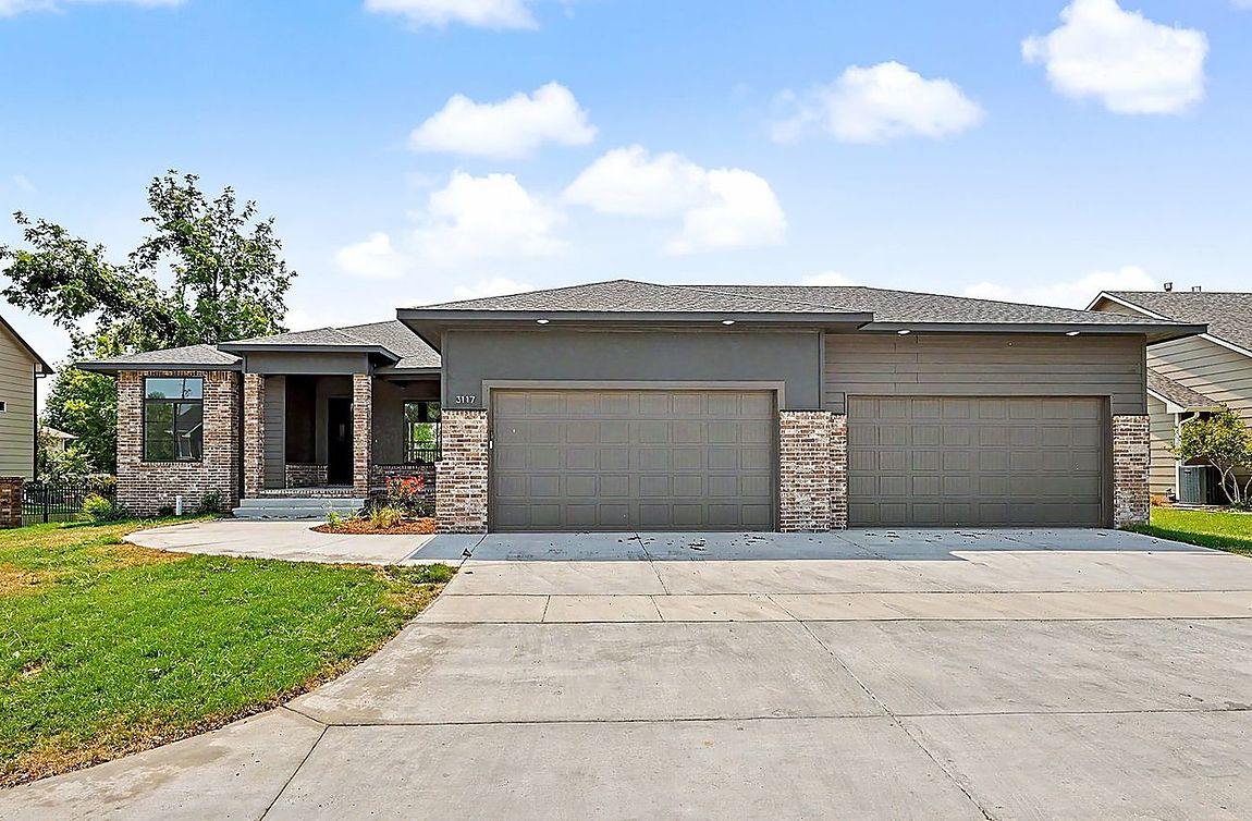 Finished RJ Castle Homes custom home with a three-car garage and manicured lawn under a blue sky – Wichita metro, KS