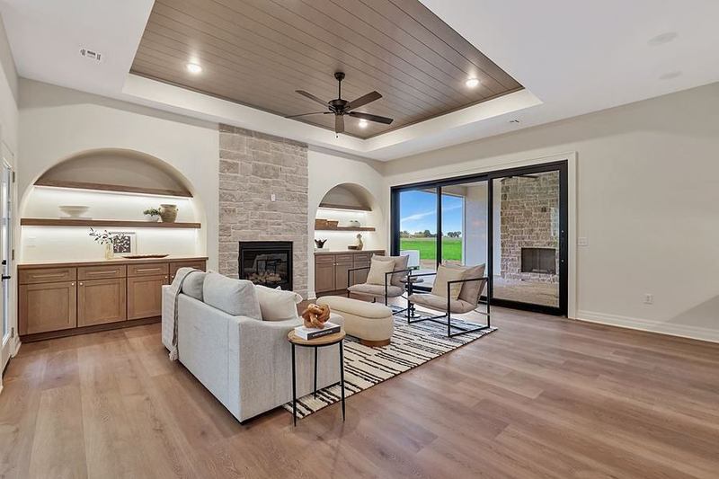 Great room with a limestone fireplace between arched lit alcoves under a planked tray ceiling at 13650 W Homestead Drive – Colwich, KS